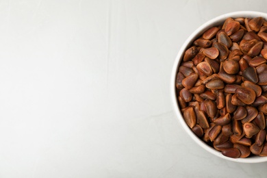 Bowl with pine nuts on light background, top view. Space for text