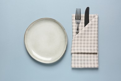 Clean plate and cutlery wrapped in napkin on light grey background, flat lay