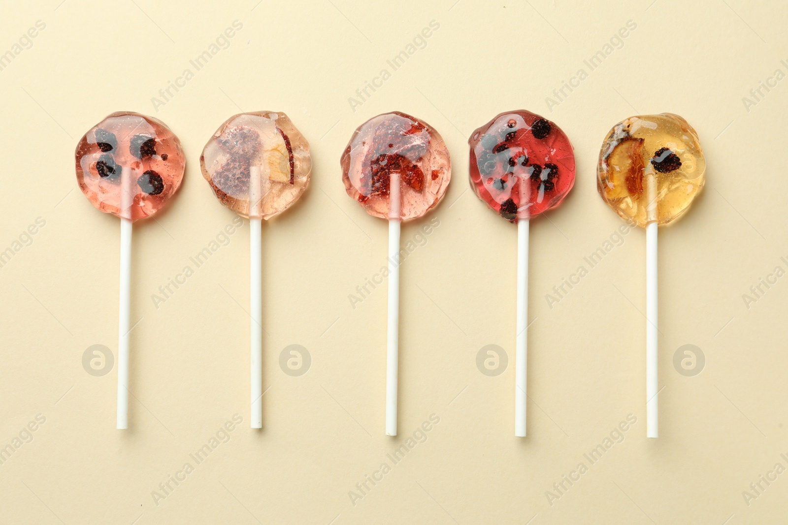 Photo of Sweet colorful lollipops with berries on beige background, flat lay