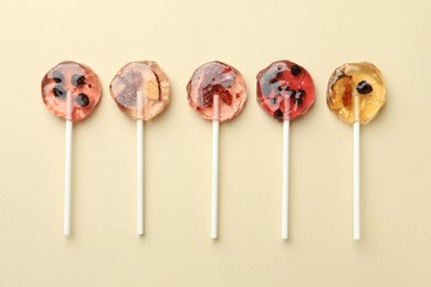 Sweet colorful lollipops with berries on beige background, flat lay