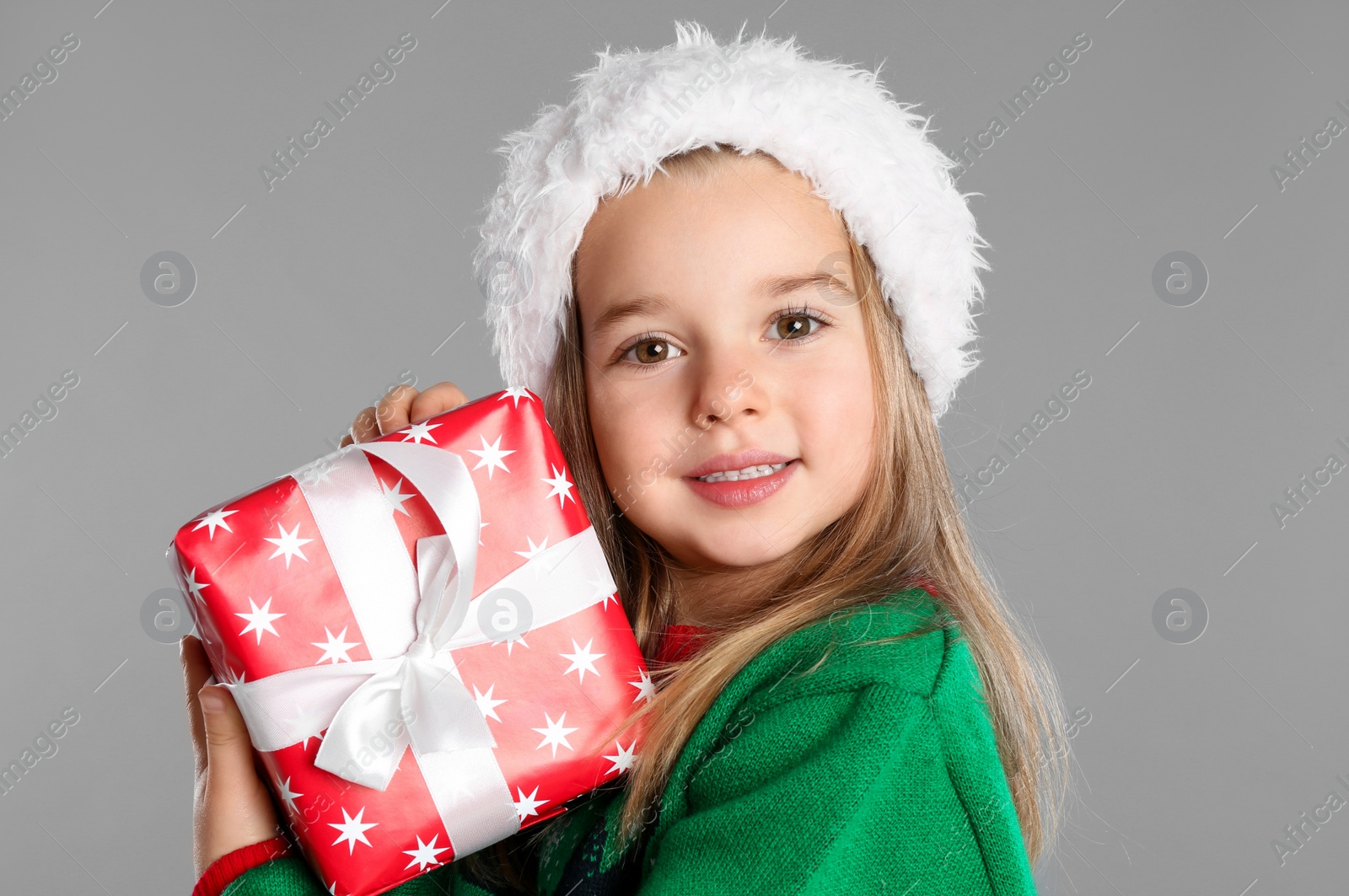 Photo of Cute child in Santa hat with Christmas gift on grey background