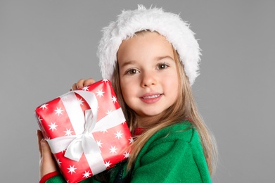 Photo of Cute child in Santa hat with Christmas gift on grey background