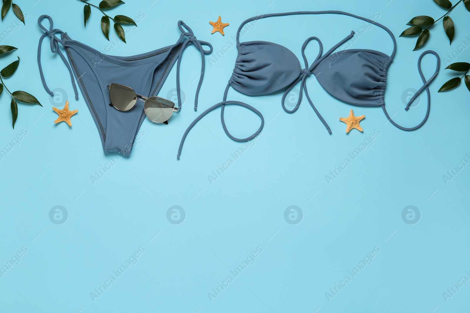 Photo of Stylish bikini, sunglasses, leaves and starfishes on light blue background, flat lay. Space for text