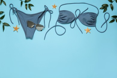 Photo of Stylish bikini, sunglasses, leaves and starfishes on light blue background, flat lay. Space for text