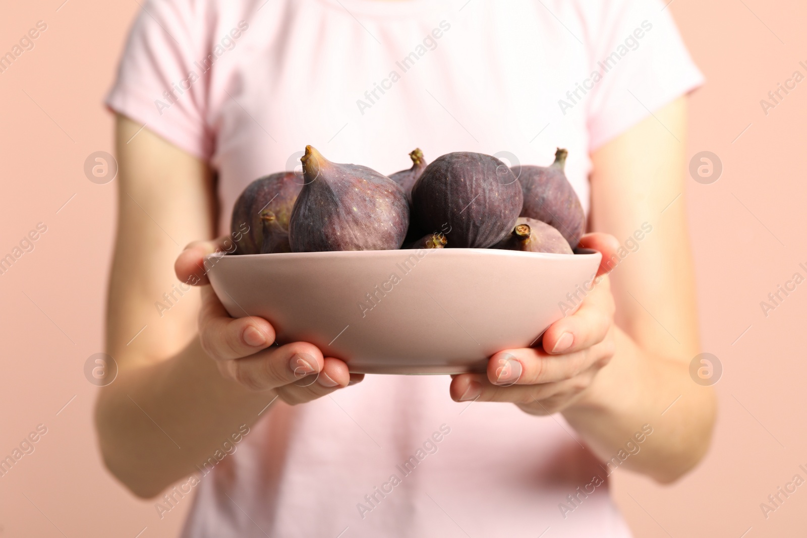 Photo of Woman holding bowl with tasty raw figs on pink  background, closeup