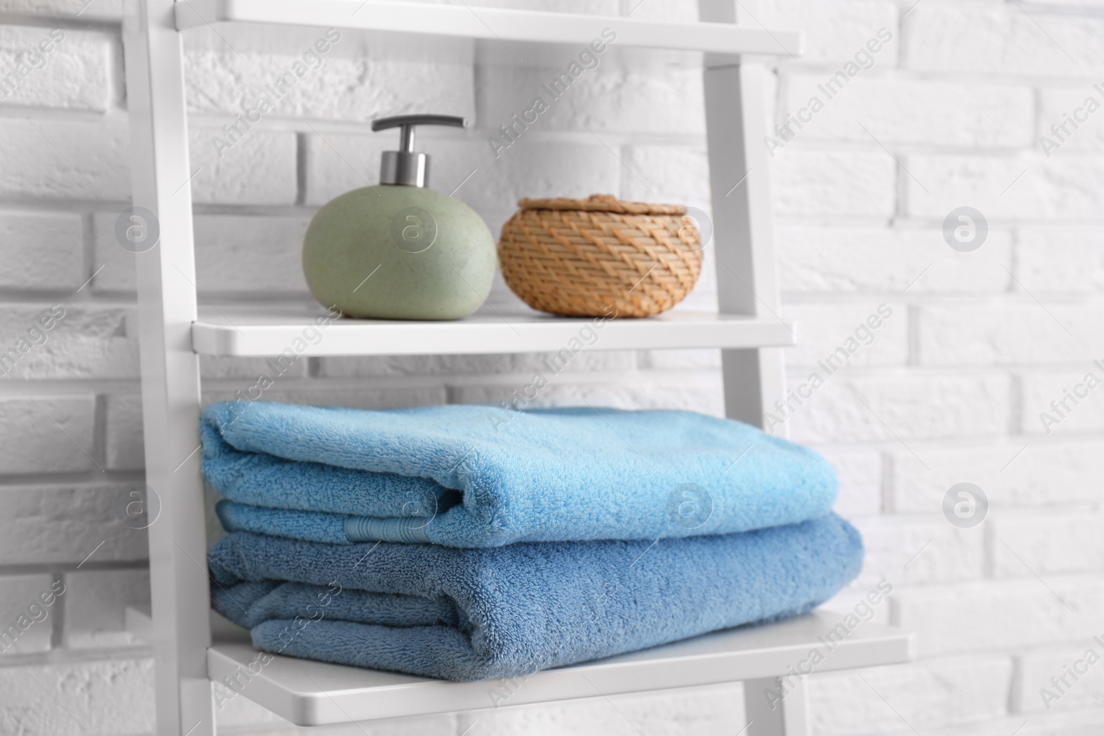 Photo of Clean soft towels and soap dispenser on shelves near white brick wall