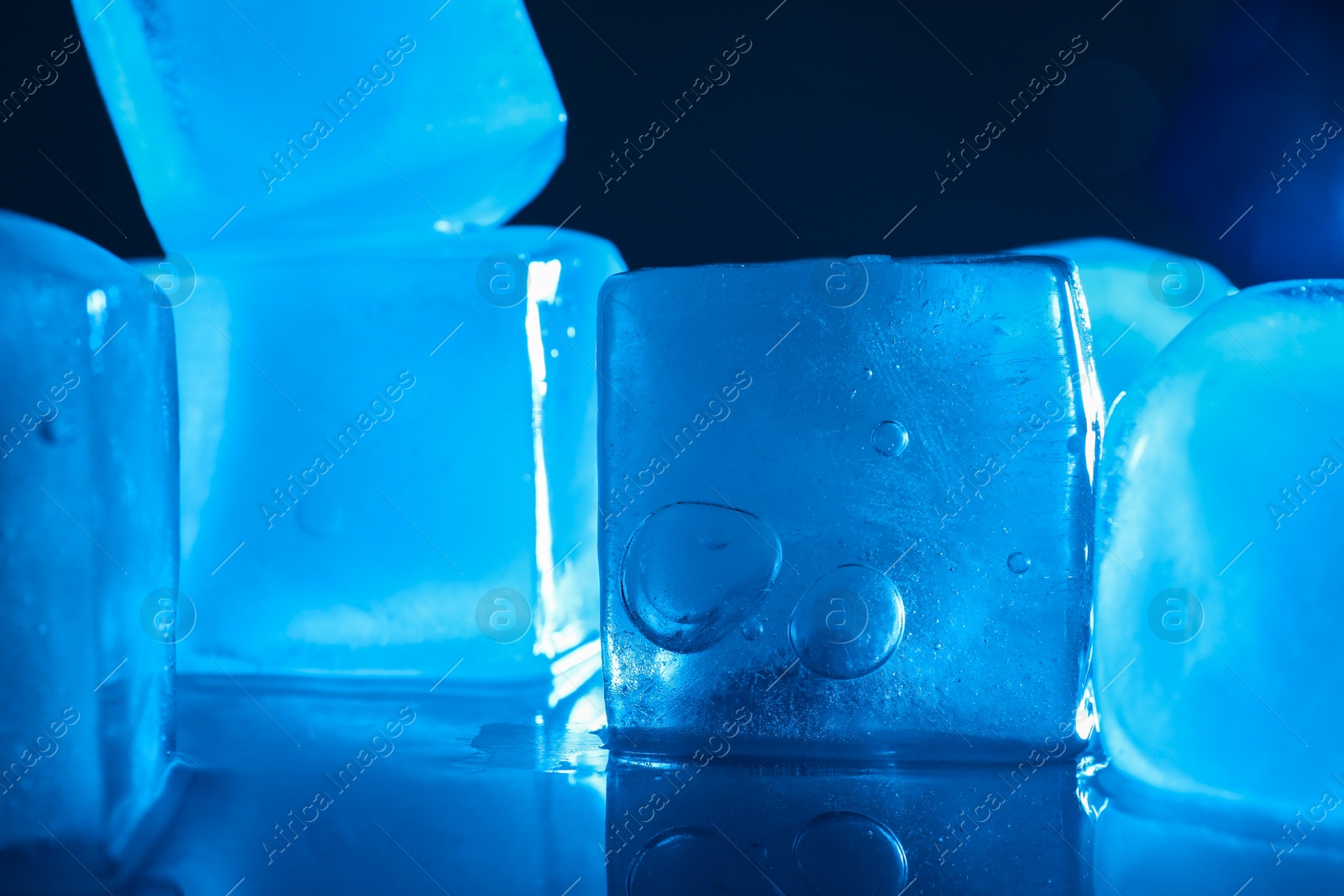 Photo of Crystal clear ice cubes on dark background, closeup. Color tone effect