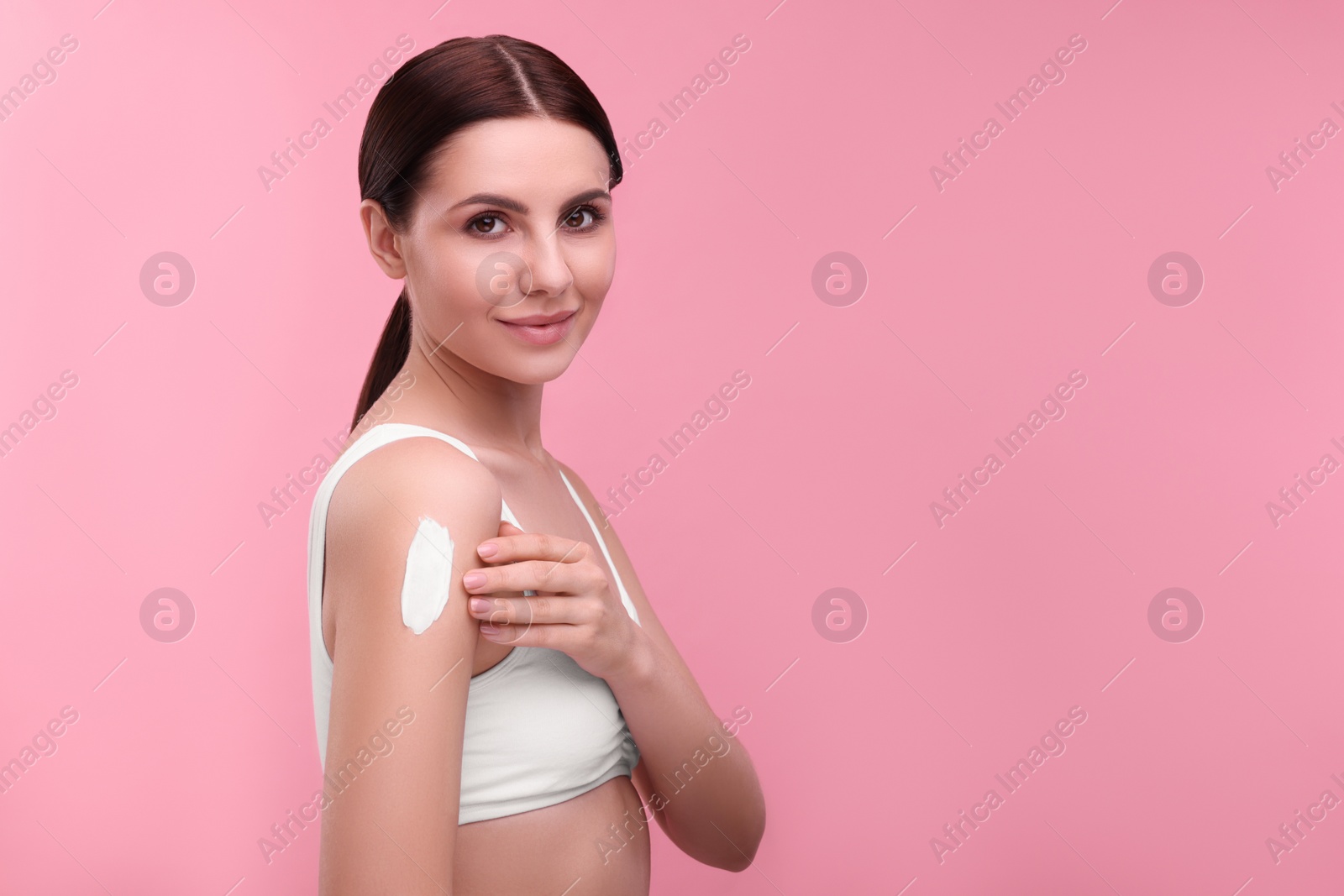 Photo of Beautiful woman with smear of body cream on her shoulder against pink background. Space for text