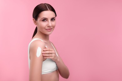 Photo of Beautiful woman with smear of body cream on her shoulder against pink background. Space for text