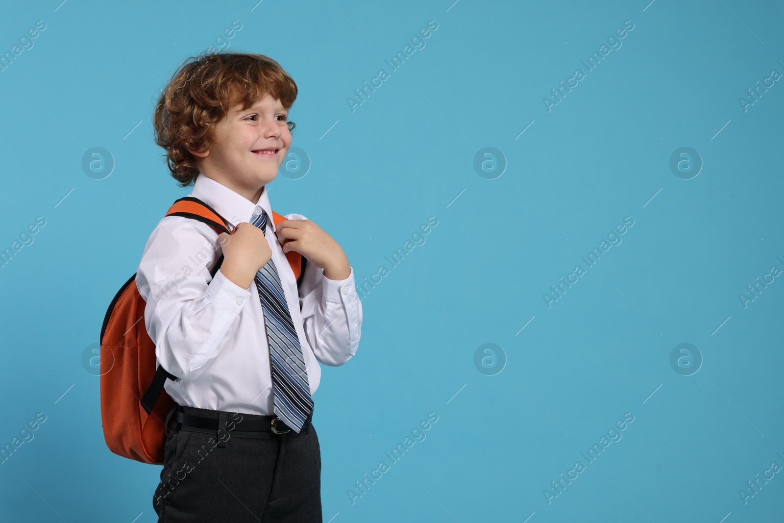 Photo of Happy schoolboy with backpack on light blue background, space for text