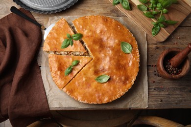 Delicious pie with meat and basil on wooden table, flat lay