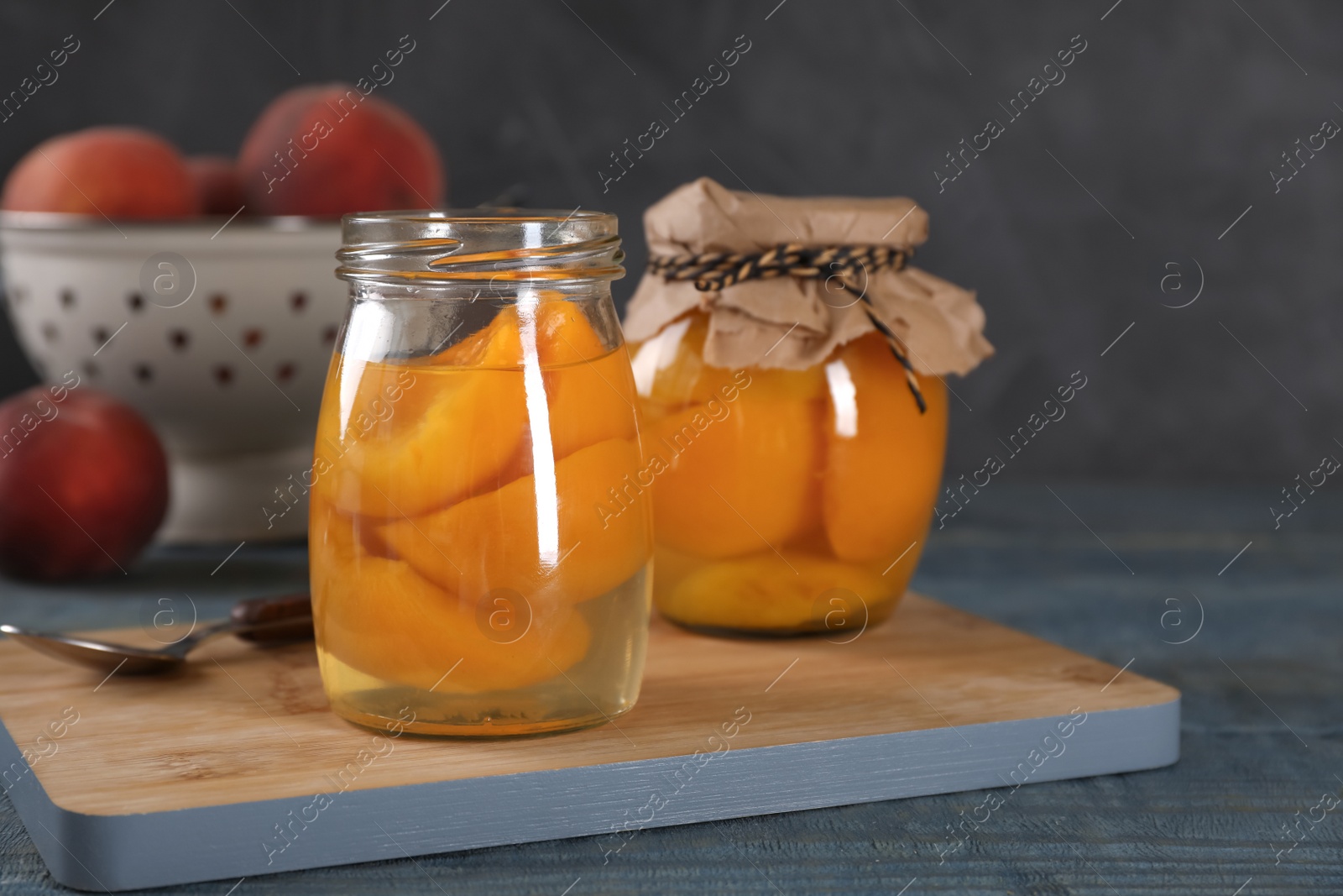 Photo of Glass jars with conserved peach halves on wooden board