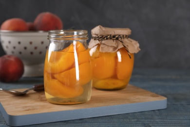 Glass jars with conserved peach halves on wooden board