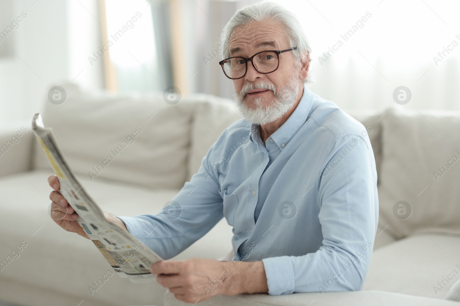 Photo of Portrait of grandpa with stylish glasses reading newspaper on sofa indoors