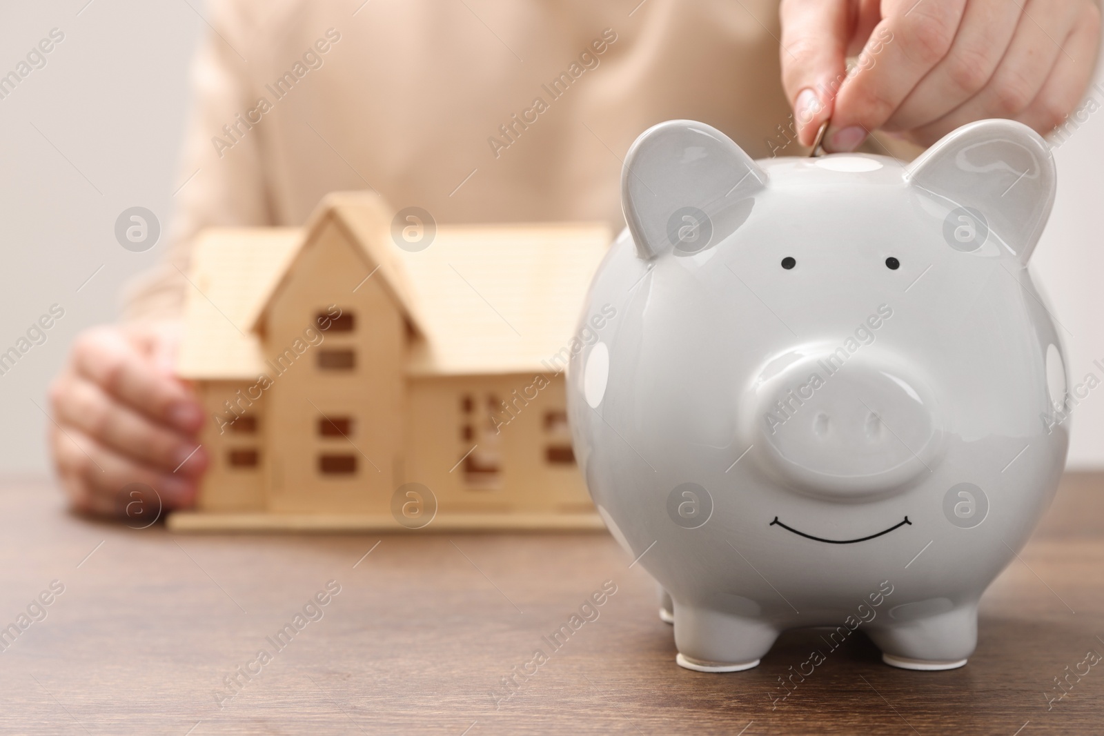 Photo of Man putting coin into piggy bank at wooden table, closeup with space for text. Saving money concept