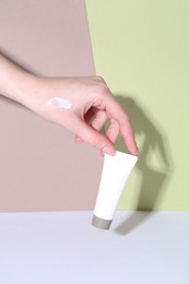 Woman with tube of cream on color background, closeup