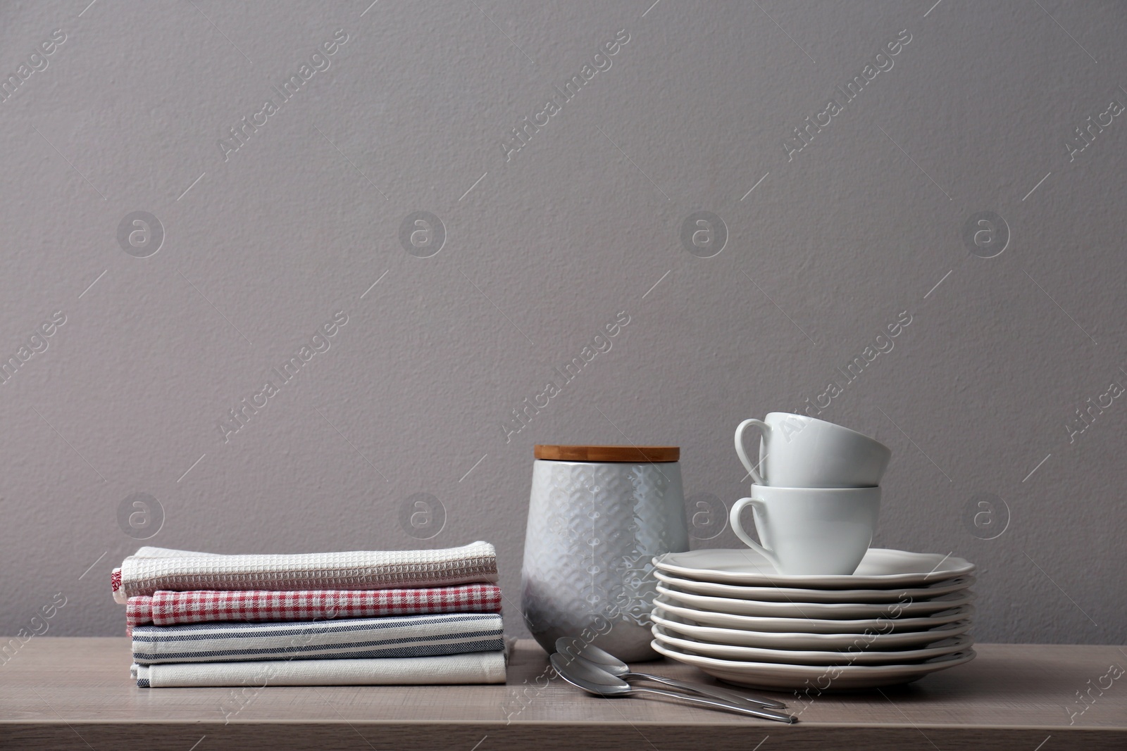Photo of Stack of soft kitchen towels and dishware on wooden table against grey background, space for text