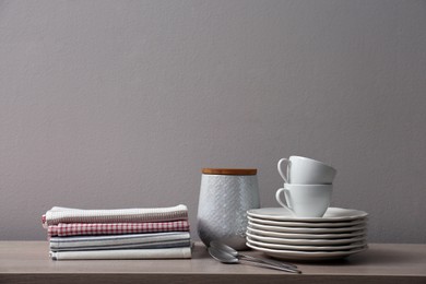 Stack of soft kitchen towels and dishware on wooden table against grey background, space for text