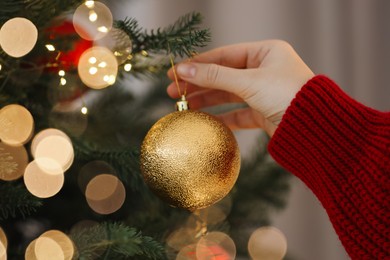 Photo of Woman decorating Christmas tree with golden festive ball on light background, closeup