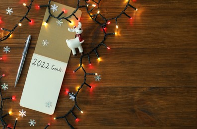 Photo of Inscription 2022 Goals written in planner and Christmas decor on wooden background, flat lay with space for text. New Year aims