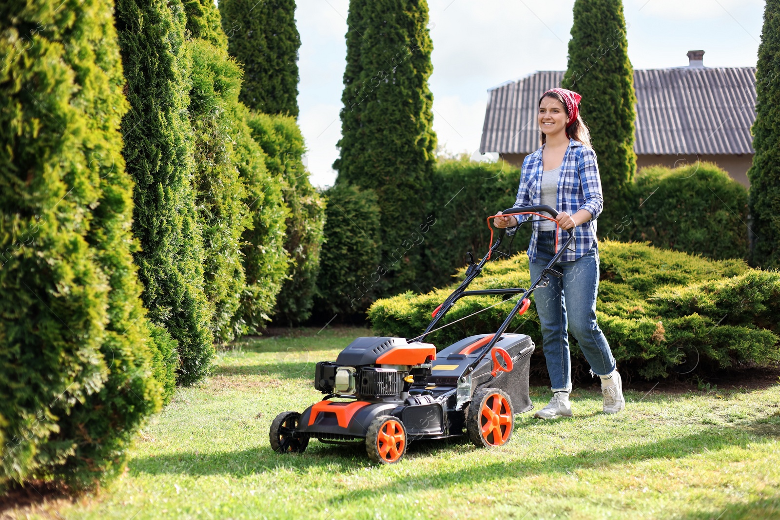 Photo of Smiling woman cutting green grass with lawn mower in garden