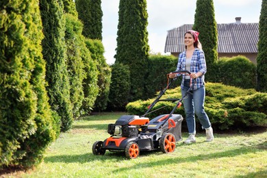 Smiling woman cutting green grass with lawn mower in garden