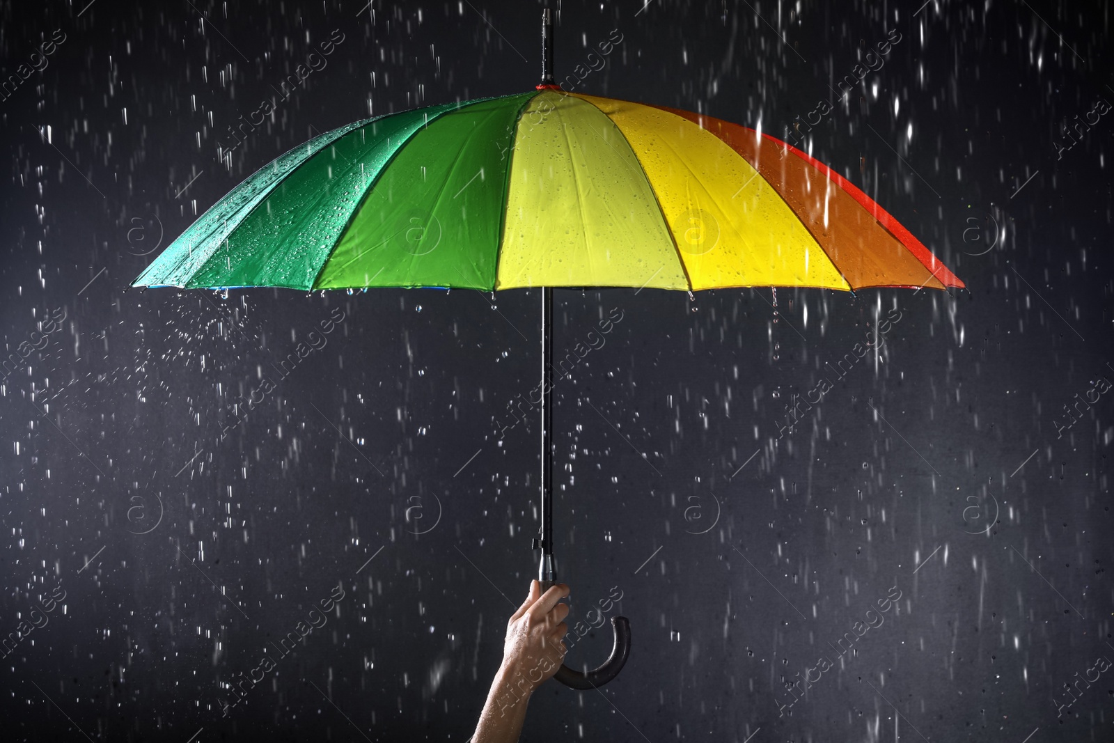 Photo of Woman holding bright umbrella under rain on dark background, closeup