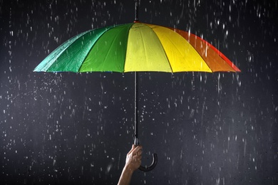 Photo of Woman holding bright umbrella under rain on dark background, closeup