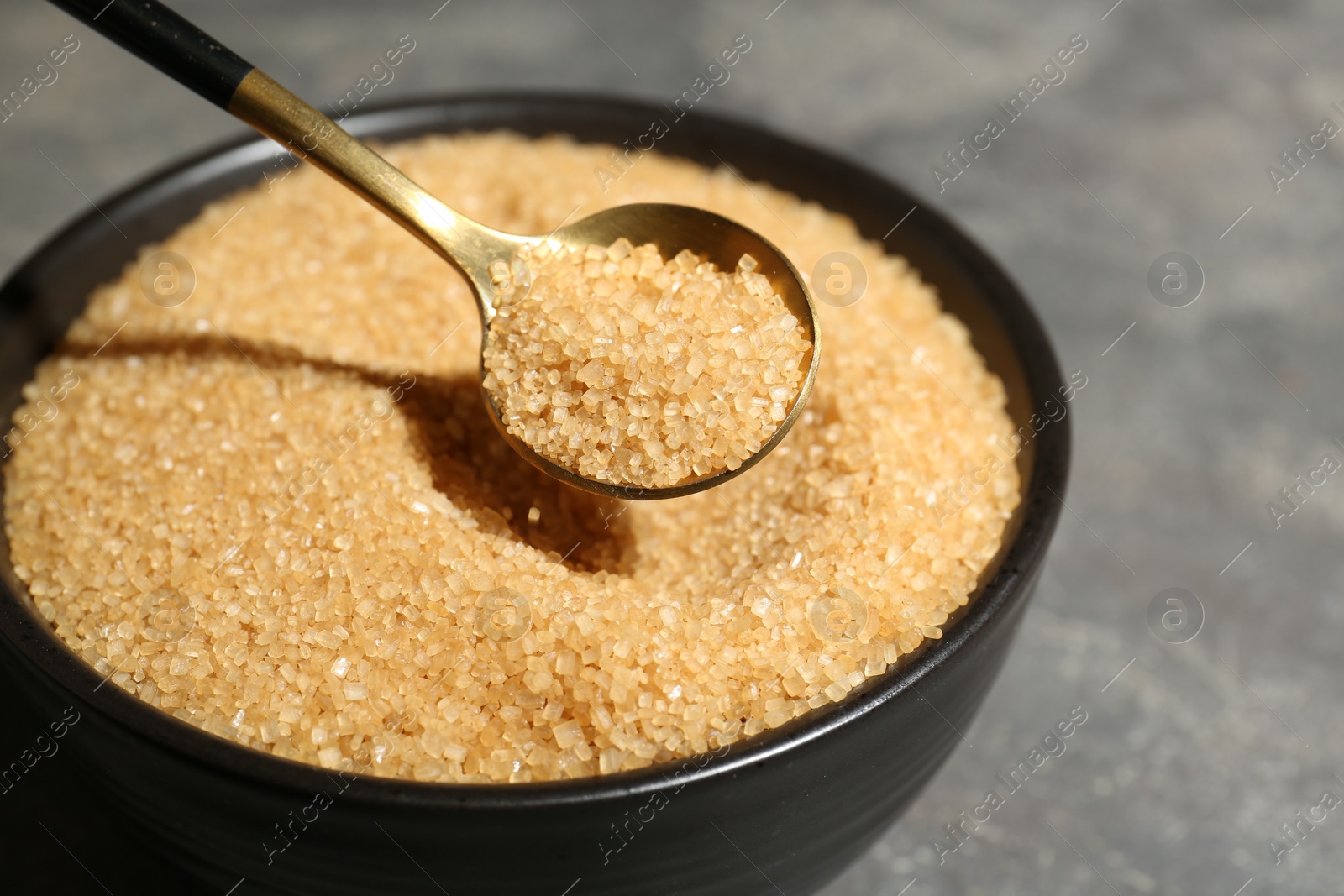 Photo of Taking brown sugar with spoon from bowl at grey table, closeup