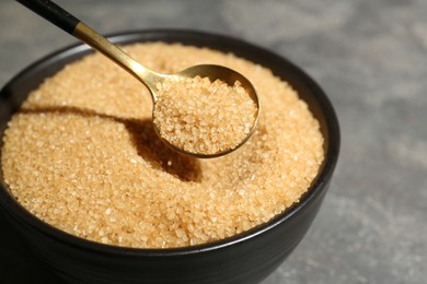 Photo of Taking brown sugar with spoon from bowl at grey table, closeup