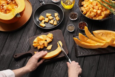 Photo of Woman cutting fresh pumpkin at black wooden table, above view