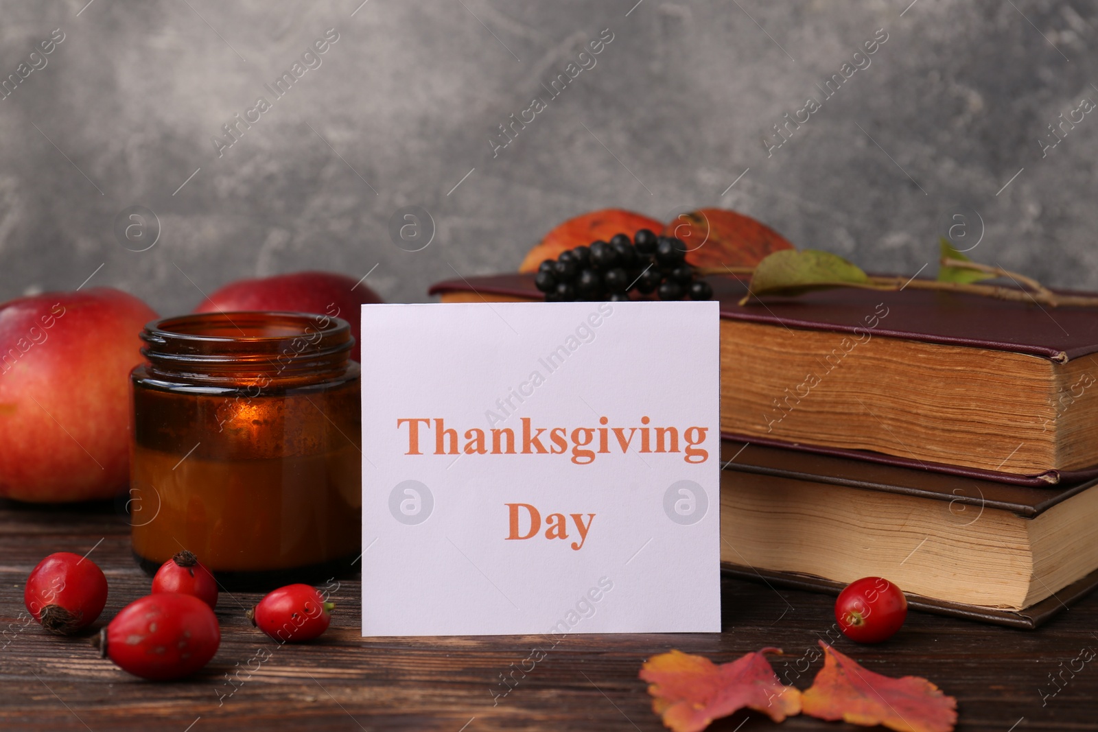 Photo of Paper card with words Thanksgiving Day near autumn leaves, berries, books and candle on wooden table