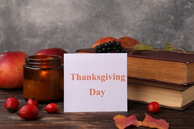 Paper card with words Thanksgiving Day near autumn leaves, berries, books and candle on wooden table