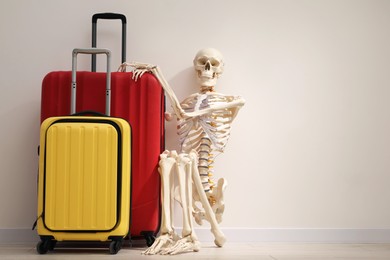 Waiting concept. Human skeleton with suitcases near light grey wall, space for text