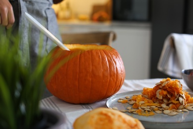 Photo of Woman making pumpkin jack o'lantern at table indoors. Halloween celebration
