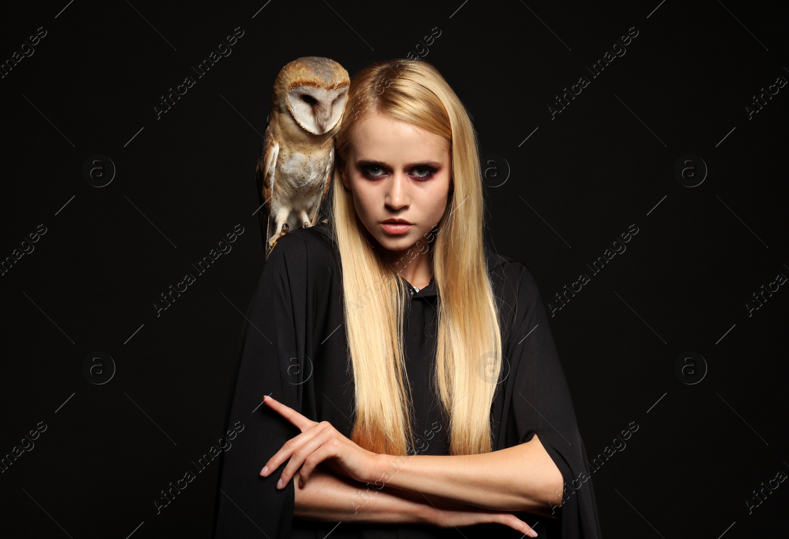 Photo of Witch in black mantle with owl on dark background. Scary fantasy character