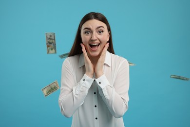 Excited woman under money shower on light blue background