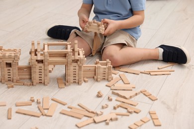 Photo of Little boy playing with wooden construction set on floor in room, closeup. Child's toy