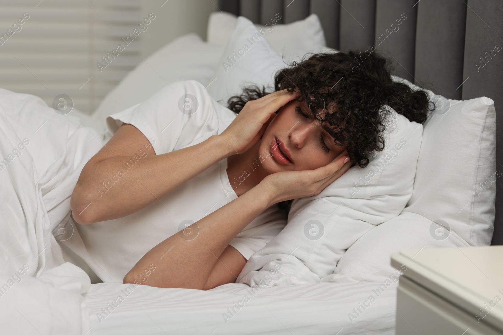 Photo of Young woman suffering from headache in bed at night