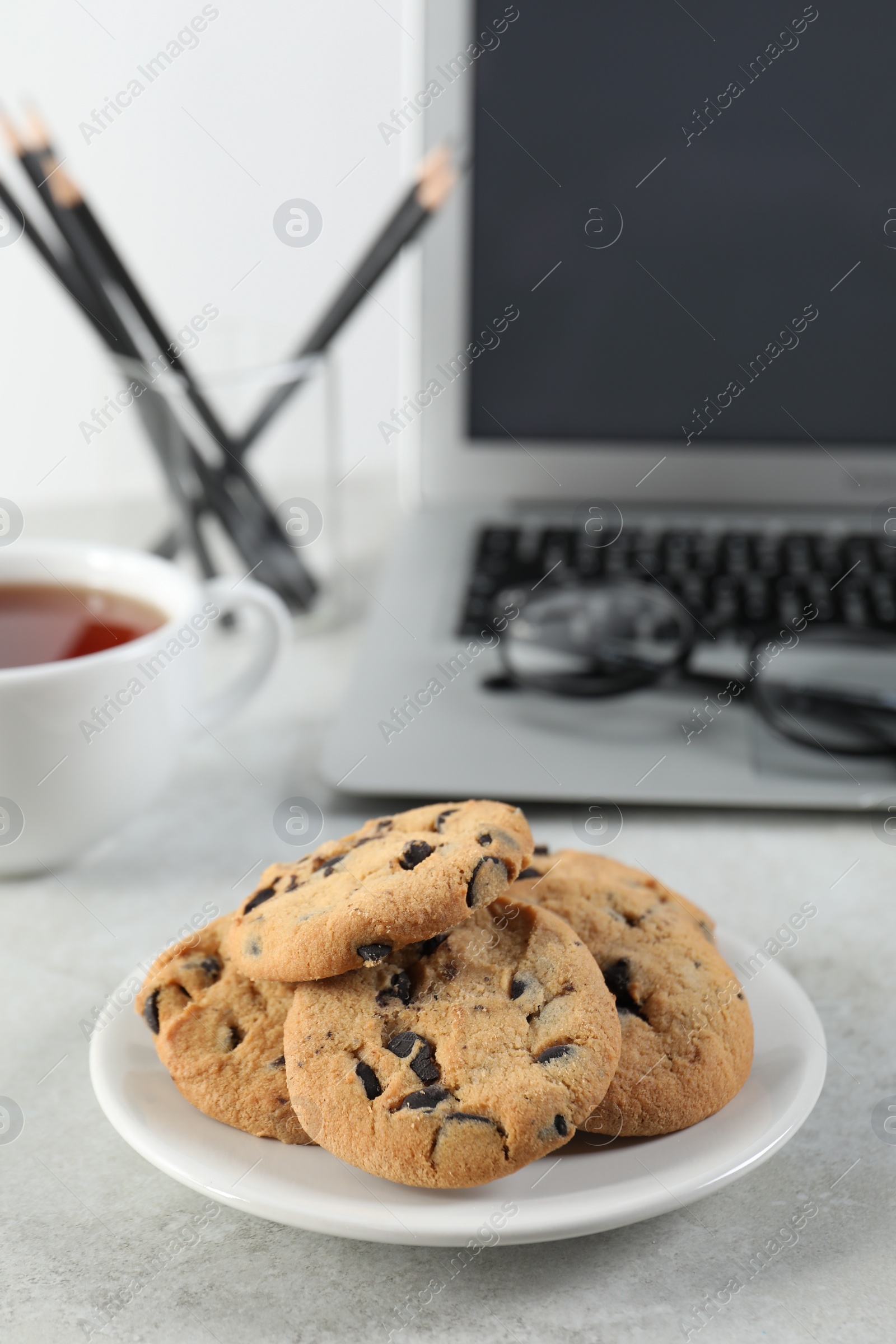 Photo of Chocolate chip cookies on light gray table at workplace