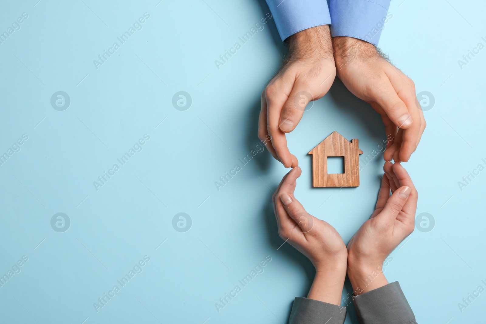 Photo of Couple holding hands near figure of house on color background, top view with space for text. Home insurance