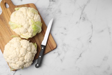 Photo of Fresh cauliflowers, cutting board and knife on white marble table, flat lay. Space for text