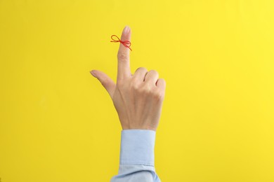 Photo of Woman showing index finger with tied red bow as reminder on yellow background, closeup