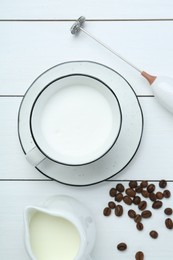 Photo of Flat lay composition with mini mixer (milk frother), whipped milk and coffee beans on white wooden table