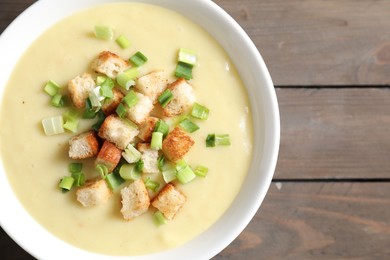 Tasty potato soup with croutons and green onion in bowl on wooden table, top view. Space for text