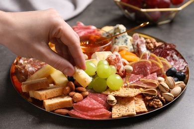 Photo of Woman taking cheese from plate with different appetizers on grey table, closeup