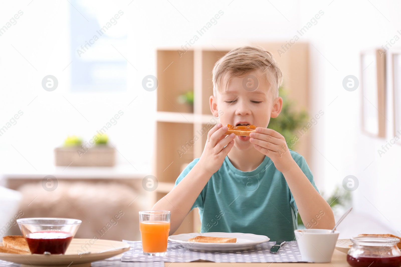 Photo of Cute little boy eating tasty toasted bread with jam at table