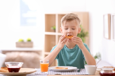 Photo of Cute little boy eating tasty toasted bread with jam at table