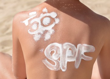 Photo of Child with abbreviation SPF 50 of sunscreen on back at beach, closeup