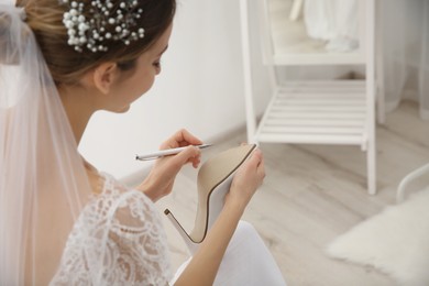 Photo of Young bride writing on her shoe indoors, closeup. Wedding superstition